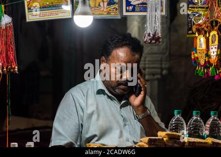 Mayiladuthurai, Tamil Nadu, India - Febbraio 2020: Un ritratto candido a bassa luce di un venditore indiano di strada illuminato da una lampadina nel suo negozio per le strade di Foto Stock