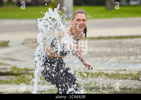 Attraente ragazza gioca felicemente con i bastoncini d'acqua fontana nel parco della città. Foto Stock