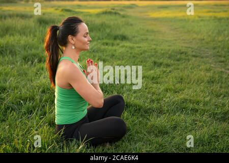 Una donna bruna di mezza età che fa yoga durante il bellissimo tramonto in un parco. Concetto di vita di salute, meditazione e relax. Foto Stock