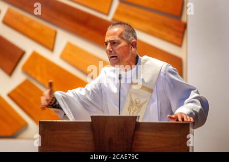 Indossando un abito bianco, un diacono entusiasta predica un sermone nel pulpito di una chiesa cattolica a Tustin, CA. Foto Stock