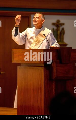 Indossando un abito bianco, un diacono entusiasta predica un sermone nel pulpito di una chiesa cattolica a Tustin, CA. Foto Stock