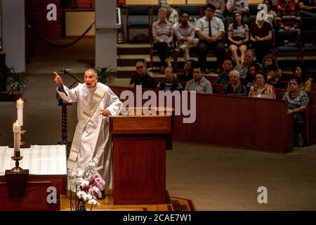 Indossando un abito bianco, un diacono entusiasta predica un sermone nel pulpito di una chiesa cattolica a Tustin, CA. Foto Stock