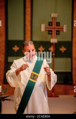 Indossando un abito bianco, un diacono entusiasta predica un sermone nel pulpito di una chiesa cattolica della California meridionale. Foto Stock