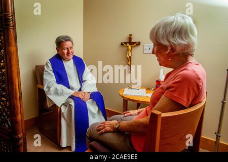 Un monsignore con canne conduce faccia a faccia la confessione con una donna anziana penitente ad una chiesa cattolica della California del sud. Foto Stock