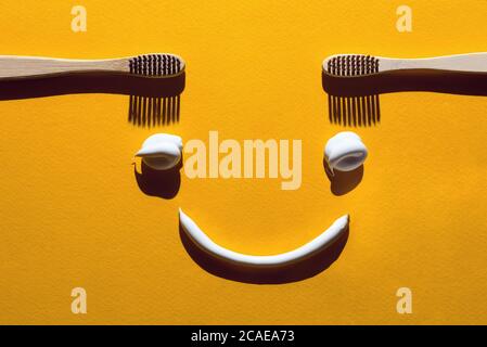 Spazzolini da denti e pasta di legno su sfondo giallo. Concetto dentale sotto forma di un volto divertente. Foto Stock