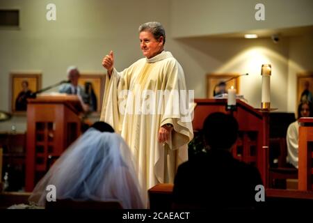 Il monsignor robato di una chiesa cattolica della California meridionale esegue una cerimonia nuziale di una sposa e uno sposo ispanici. Foto Stock