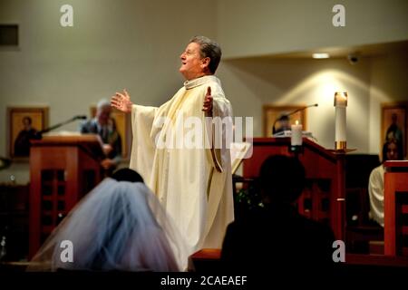 Il monsignor robato di una chiesa cattolica della California meridionale esegue una cerimonia nuziale di una sposa e uno sposo ispanici. Foto Stock