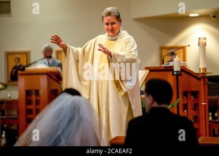 Il monsignor robato di una chiesa cattolica della California meridionale esegue una cerimonia nuziale di una sposa e uno sposo ispanici. Foto Stock