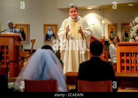 Il monsignor robato di una chiesa cattolica della California meridionale esegue una cerimonia nuziale di una sposa e uno sposo ispanici. Foto Stock