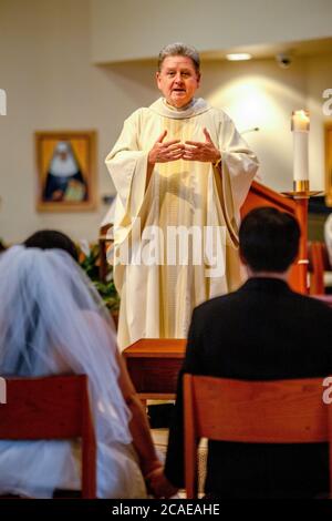 Il monsignor robato di una chiesa cattolica della California meridionale esegue una cerimonia nuziale di una sposa e uno sposo ispanici. Foto Stock