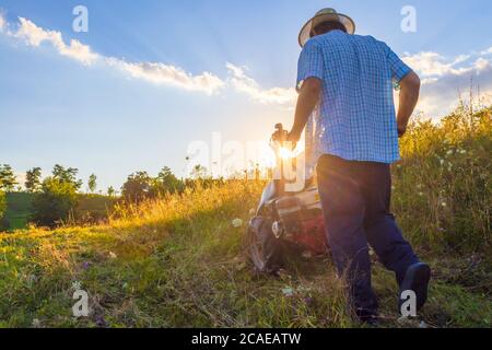 Estate fattoria Scenic. Uomo Seniour che aziona il rasaerba a barra di falcola nel campo Foto Stock