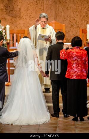 Il monsignor robato di una chiesa cattolica della California meridionale esegue una cerimonia nuziale di una sposa e uno sposo ispanici. Foto Stock