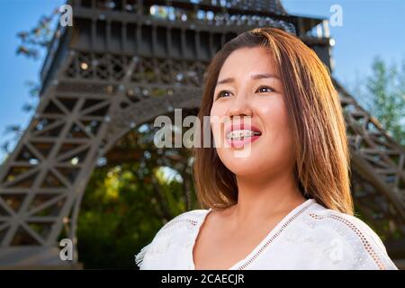 Una ragazza di aspetto asiatico in una T-shirt bianca guarda al lato e sorride sui suoi denti dentali bretelle Foto Stock