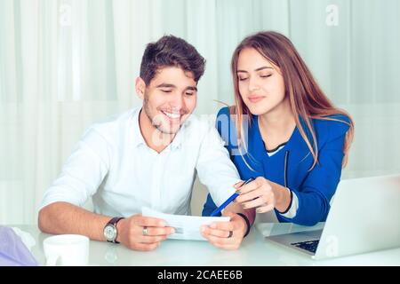 Giovane donna intelligente che punta con la penna su carta mostrando informazioni al giovane uomo collega che lavora in squadra. Felice coppia colleghi che condividono il lavoro siedono Foto Stock