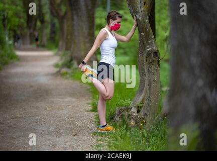 Mantenersi in forma durante il Coronavirus. Una donna sportiva sta facendo jogging all'aperto, ha una maschera protettiva sul viso. In esecuzione nei giorni del Covid-19. Foto Stock