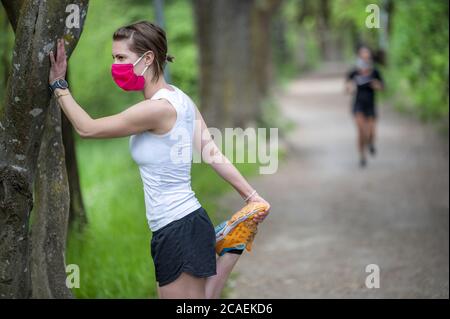 Mantenersi in forma durante il Coronavirus. Una donna sportiva sta facendo jogging all'aperto, ha una maschera protettiva sul viso. In esecuzione nei giorni del Covid-19. Foto Stock