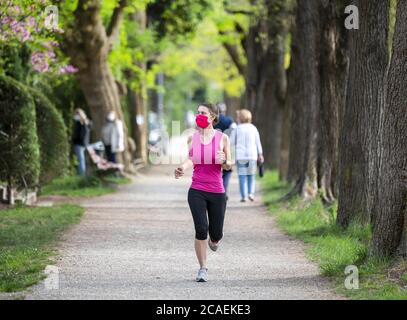 Mantenersi in forma durante il Coronavirus. Una donna sportiva sta facendo jogging all'aperto, ha una maschera protettiva sul viso. In esecuzione nei giorni del Covid-19. Foto Stock