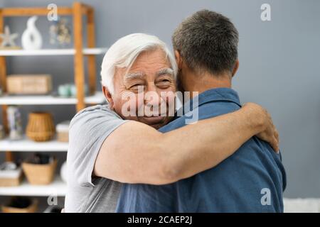 Figlio abbracciando il suo felice Padre Senior in interni Foto Stock