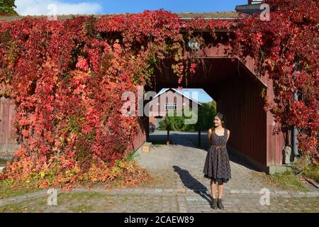 Giovane donna asiatica felice che pensa contro il passaggio di legno coperto in piante superriduttore di elegante casa suburbana Foto Stock