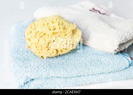 Una spugna gialla naturale su asciugamani impilati su un tavolo di legno bianco. Cura personale e igiene. Bagno e relax Foto Stock