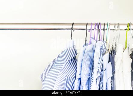 Un gruppo di camicie da uomo di vari colori appese con appendiabiti all'interno di un armadio. Moda e abbigliamento. Foto Stock