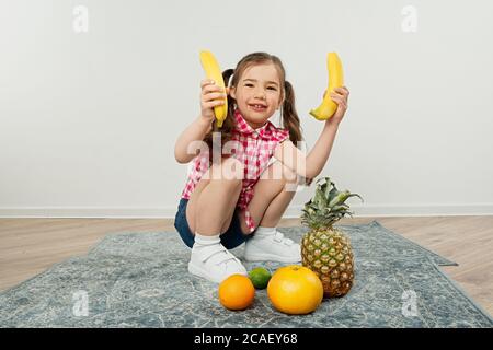 ragazza carina di capretto che tiene le banane in mano, giocando con la frutta Foto Stock