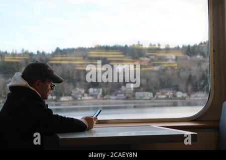 Il passeggero che sta testando e guardando il suo telefono cellulare mentre si fa un giro in traghetto a Seattle. Foto Stock