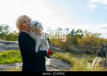 Donna anziana che osserva scioccata mentre tiene il cane su masso nelle montagne Foto Stock