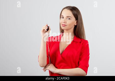 ragazza in abiti rossi tiene l'attrezzo per trucco permanente, ritratto di ragazza con sorriso, mаster su sfondo grigio contiene un apparecchio per microlavatura e. Foto Stock