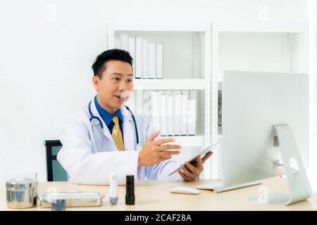 Il medico asiatico indossa cappotto bianco e cuffie che parlano videoconferenza sul computer portatile utilizzando l'app di consultazione delle videochiamate online. H. Medico remoto Foto Stock