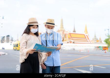 Coppie asiatiche turisti felici di viaggiare indossando maschera per proteggere da Covid-19 su loro vacanze e tenendo la mappa di viaggio in Wat Phra Kaew Tempio a Bangkok Foto Stock