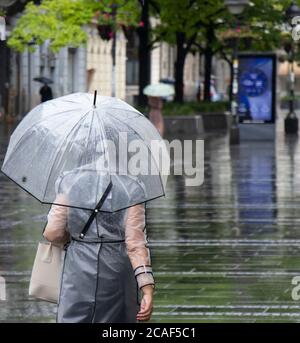 Donna in impermeabile trasparente che cammina sotto ombrello in una giornata estiva piovosa nella città di Belgrado, Serbia Foto Stock