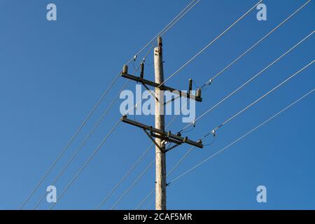 Palo telefonico in legno e linee elettriche con sfondo blu del cielo. Foto Stock