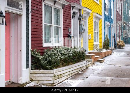 Esterno di numerose case a schiera adiacenti dai colori vivaci con grandi finestre e porte. C'è neve a terra e sul marciapiede vicino agli edifici. Foto Stock