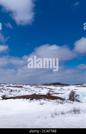 Inverno su una collina arida e paludosa. L'erba gialla sta puntando su attraverso i moounds.The bianchi di neve lo sfondo è cielo blu con le nuvole fluide bianche. Foto Stock