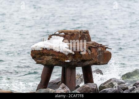 Un vecchio bacino vicino al bordo dell'oceano. Il molo di sterzo arrugginito è parzialmente sommerso in acqua e la parte in piedi ha neve su di esso. Foto Stock