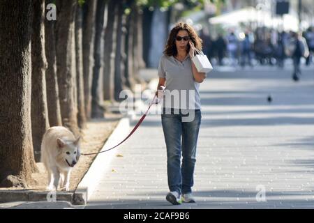 Donna che cammina il suo cane e parla al telefono in Piazza Umberto i, Via Sparano da Bari. Bari, Italia Foto Stock