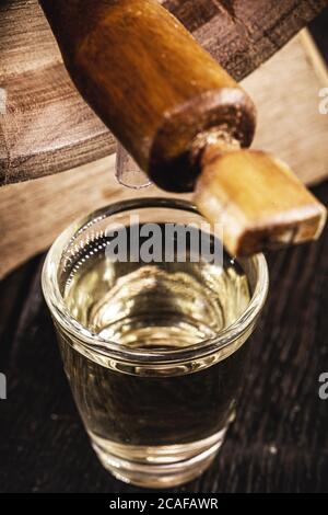 bicchieri per piccole dosi, alcol distillato di alta qualità. cachaça brasiliano (chiamato pinga), gocciolamento, con legno rustico brasile, immagine bar, vecchia cantina. Foto Stock