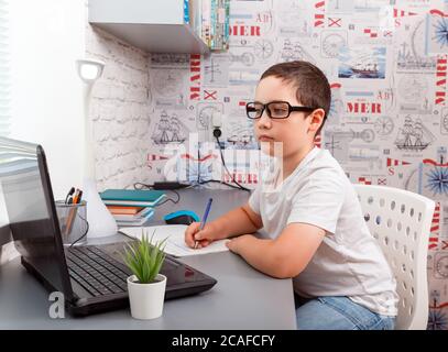 Bambino che usa il computer portatile mentre si siede alla scrivania con libro e si fa il lavoro Foto Stock