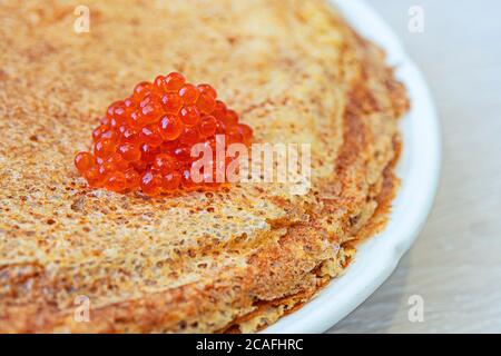 Tradizionali frittelle russe con caviale rosso su piatto bianco un tavolo di legno Foto Stock