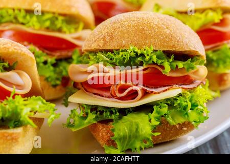 Panini colorati con prosciutto, verdure e formaggio su piatto bianco su sfondo di legno. Foto Stock