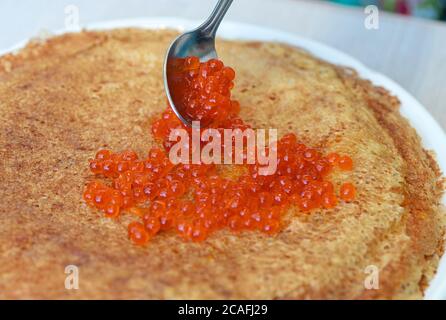 Pancake con caviale rosso su un piatto. Accanto ai pancake c'è un cucchiaio con caviale. Sfondo chiaro. Primo piano. Foto Stock
