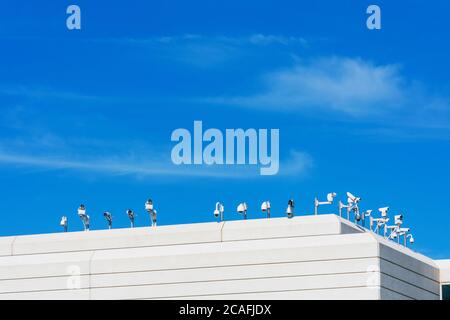 Varie telecamere di sicurezza esterne coprono diverse angolazioni dal tetto di un moderno edificio d'uffici sotto il cielo blu Foto Stock