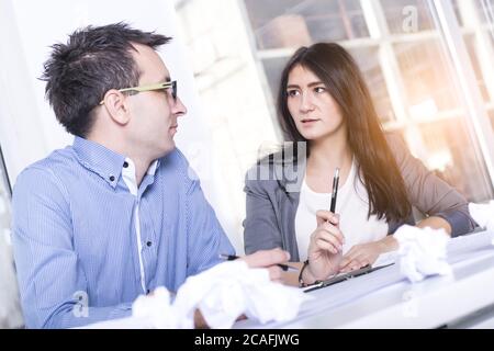 Primo piano di due partner commerciali caucasici che discutono di lavoro mentre si siedono dietro la scrivania Foto Stock