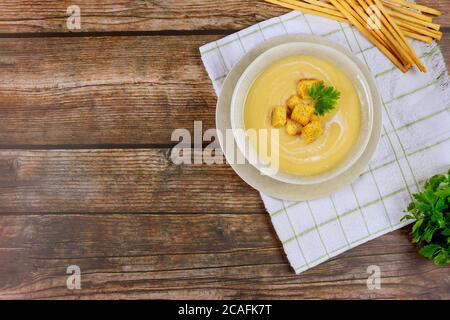Zuppa di verdure fresche e cremose in ciotola grigia guarnita con crostini croccanti e bastoncini di pane italiani. Foto Stock