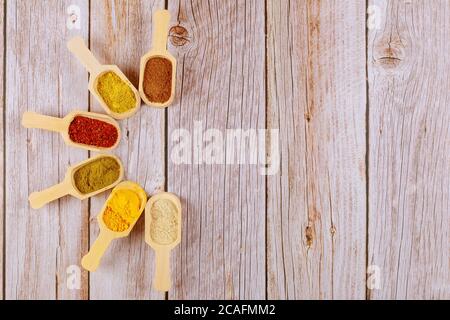 Spezie macinate colorate polveri in cucchiai di legno su sfondo bianco di legno. Foto Stock