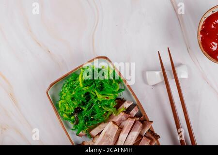 Fette di carne di maiale alla griglia in stile giapponese con alghe, salsa e chopstick Foto Stock