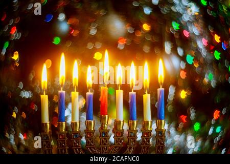 Menorah con candele brucianti per Hanukkah su sfondo scintillante con luci colorate sfocate. Festa ebraica. Foto Stock