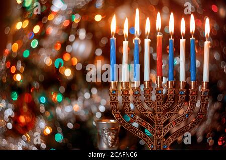 Candele brucianti con menorah per Hanukkah su sfocare colore luci di sfondo. Festa ebraica Foto Stock