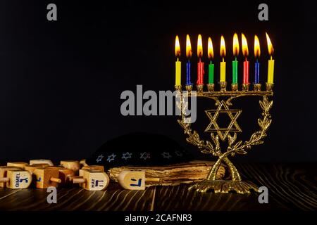 Menorah con candele a colori e Dreidel su sfondo nero. Foto Stock